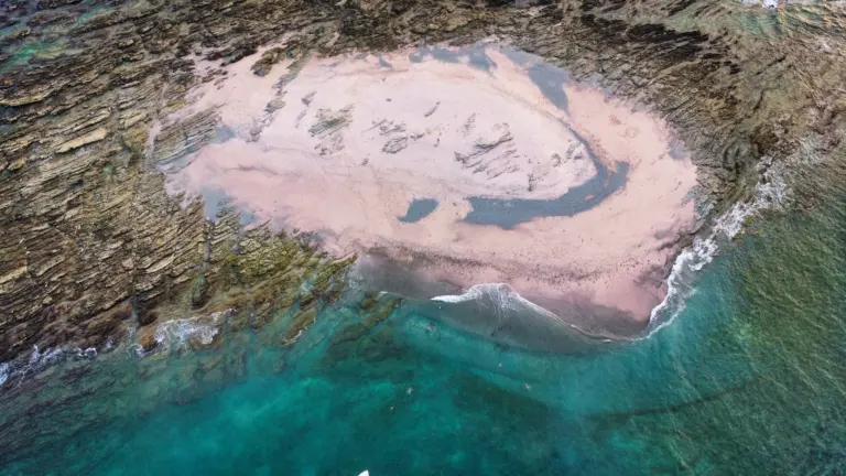 Aerial close-up of the sandbar exposed at low tide inside its ring of dark rock near Nosara.