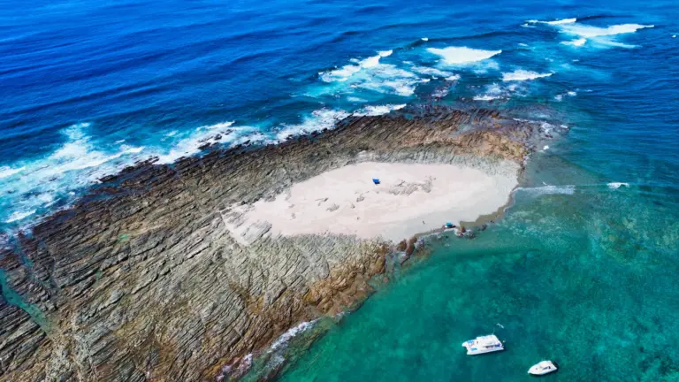 Aerial view of the Pink Island sandbar ringed by rock ledges with a catamaran anchored nearby.