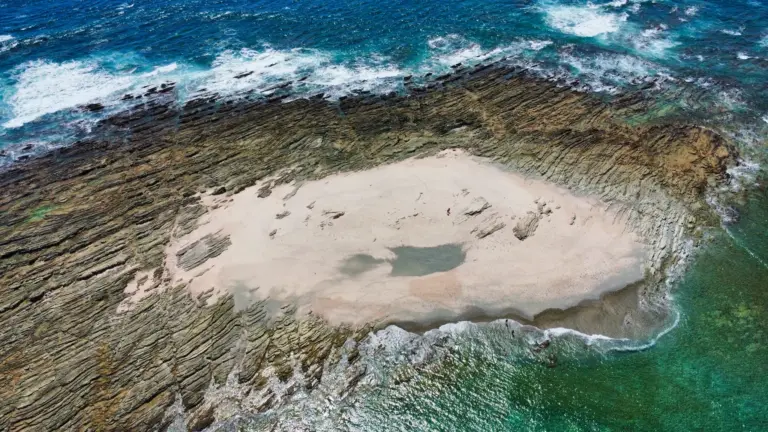 Aerial view of a pale sandbar surrounded by dark rock shelves and breaking surf near Nosara.