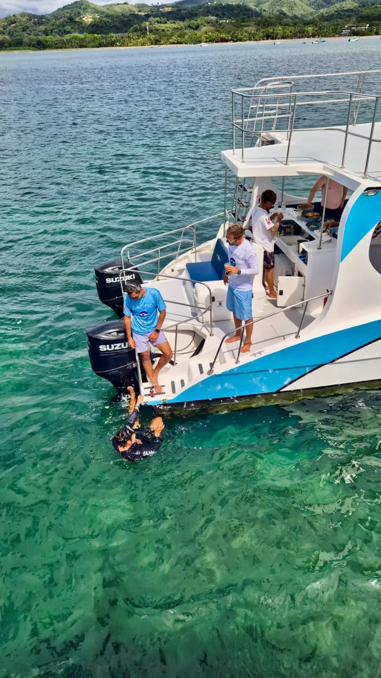 Guests climb down the boat's ladder into clear green water to start snorkeling near Nosara.