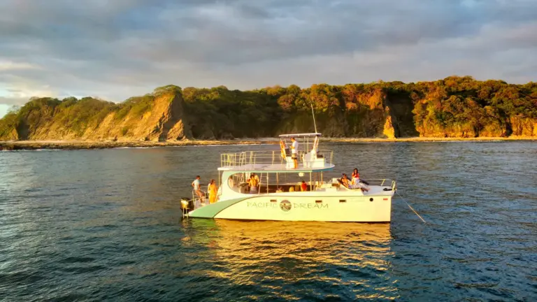 The catamaran sits at anchor below green cliffs on the Guanacaste coast in evening light.