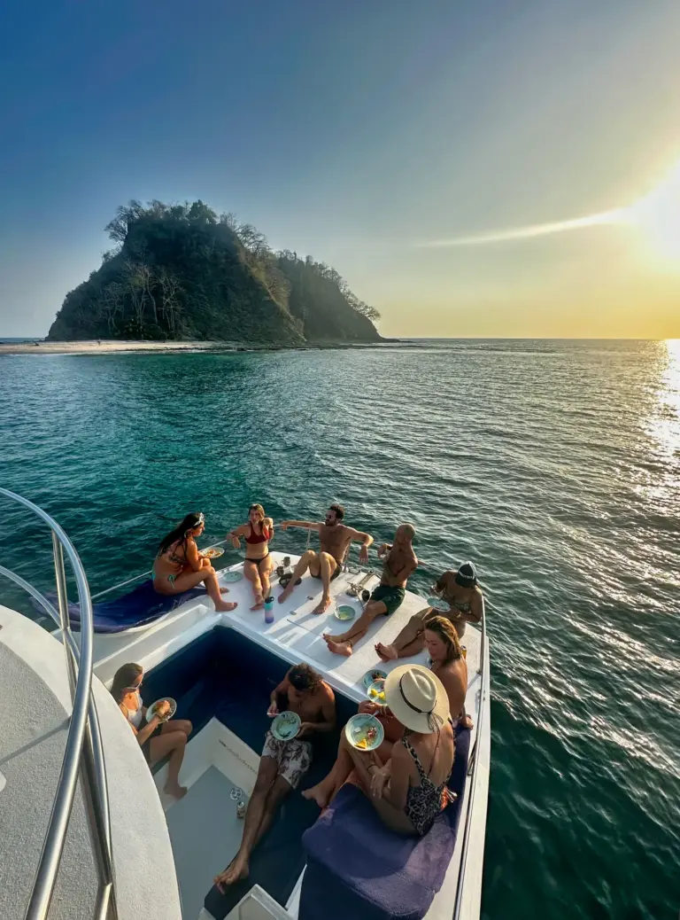 Guests relax on the bow as the catamaran passes a green rock island off the Nosara coast.
