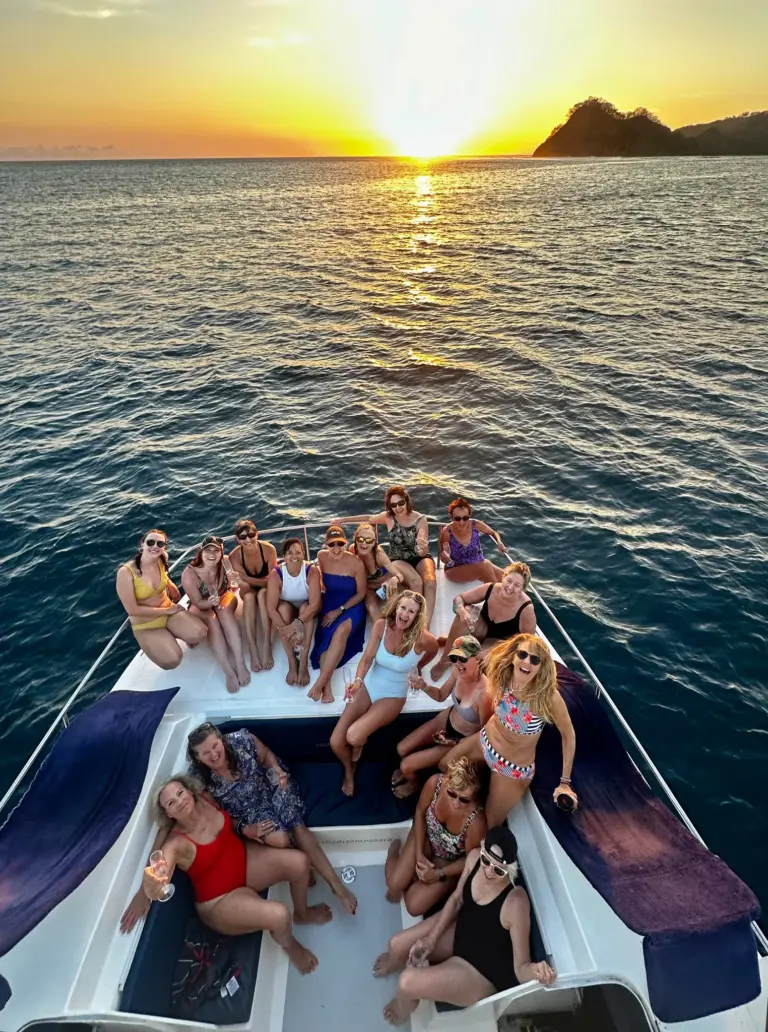 Overhead view of guests filling the catamaran's bow as the sun sets behind an island.