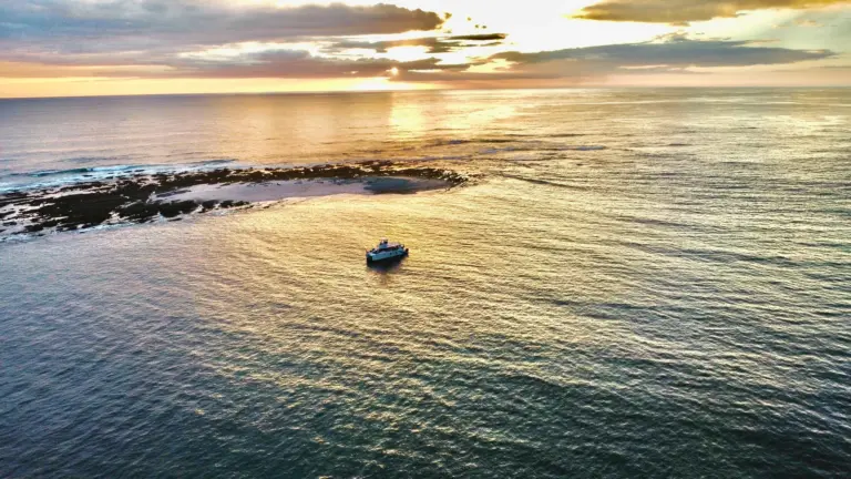 Aerial view of a rocky reef and a small boat on calm golden water near Nosara.