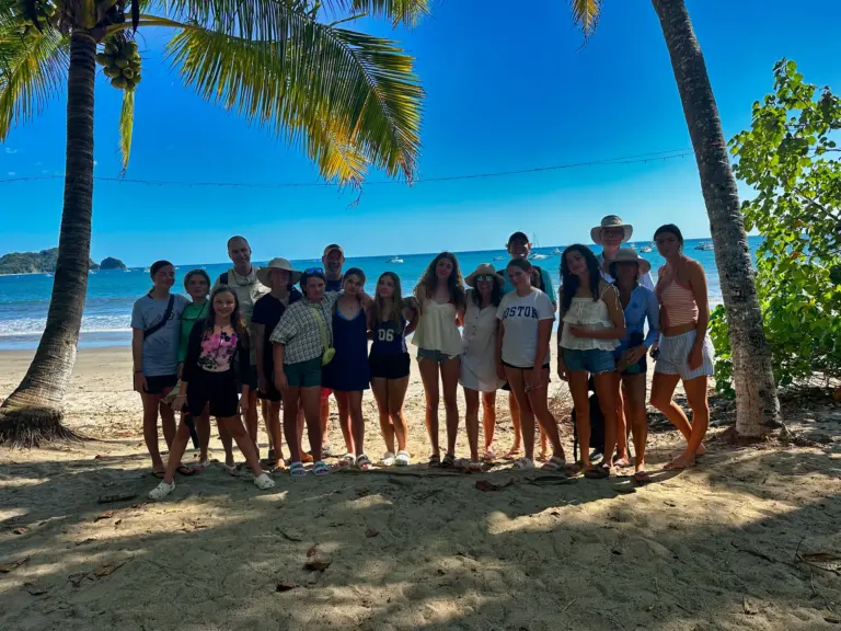 A large group lines up on the sand under the palms before boarding at Playa Garza, Nosara.