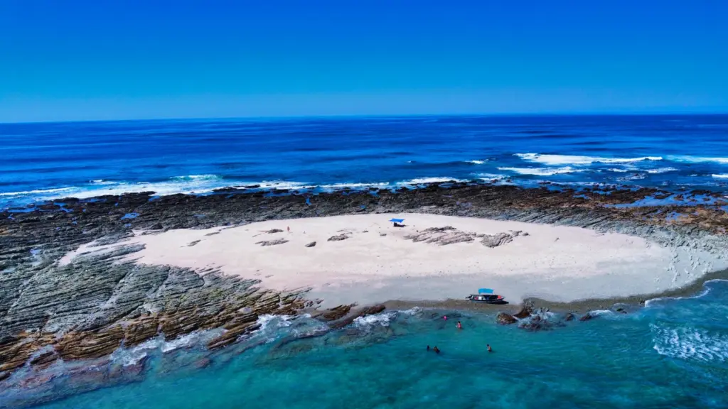 Aerial view of a small white sand island ringed by reef and turquoise water near Nosara.