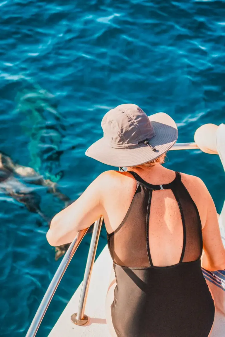 A guest leans on the rail watching dolphins swim through the clear water below the boat.